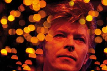 La locandina è dominata da un primo piano del volto di David Bowie, che occupa la parte superiore dell'immagine. Ha i capelli rossastri e lo sguardo diretto verso l'osservatore, con un'espressione enigmatica. Lo sfondo dietro di lui è sfocato e presenta delle luci calde e bokeh, creando un'atmosfera suggestiva. Sotto l'immagine di David Bowie, in caratteri grandi e neri, spicca la scritta "GUIDO HARARI". Subito sotto, in un colore arancione bruciato e con un carattere leggermente diverso, si legge "TOWER OF SONG".
Più in basso, in nero, sono indicate le date e il luogo dell'evento: "13 GIUGNO - 12 OTTOBRE 2025" e "CASTELNUOVO MAGRA TORRE DEL CASTELLO DEI VESCOVI DI LUNI". In una sezione successiva, divisa in due colonne, sono presenti informazioni su orari, biglietti e contatti. A sinistra, gli orari di apertura divisi per mesi (GIUGNO, SETTEMBRE, OTTOBRE e LUGLIO, AGOSTO) con indicazioni per giorni feriali e festivi. A destra, le informazioni sui biglietti ("Biglietti: Intero € 7,00, Ridotto € 5,00") e i contatti per informazioni e prenotazioni (indirizzo email e numero di telefono).
Nella parte inferiore della locandina sono presenti diversi loghi di sponsor o enti patrocinanti, tra cui "Bandiera Arancione", "Castelnuovo Magra", "Wall Of Sound Gallery" e altri
