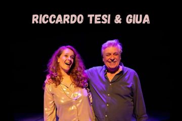 L'immagine è un poster che annuncia l' evento musicale. In alto, in caratteri bianchi, è scritto "RICCARDO TESI & GIUA".
Al centro, due persone sono ritratte sorridenti. Un uomo più anziano, con i capelli grigi e una camicia scura, tiene il braccio attorno alle spalle di una donna più giovane, che indossa una camicia chiara e lucida. Entrambi guardano verso la fotocamera e sembrano felici. Sotto, in caratteri gialli, si legge il titolo dell'evento: "Retablos", seguito da una frase descrittiva: "Bottoni, corde, canzoni e finestre". Infine, in basso, sempre in giallo, ci sono i dettagli della location e dell'orario: "PIAZZA QUERCIOLA, CASTELNUOVO MAGRA (SP) ORE 21:30". Lo sfondo è scuro.