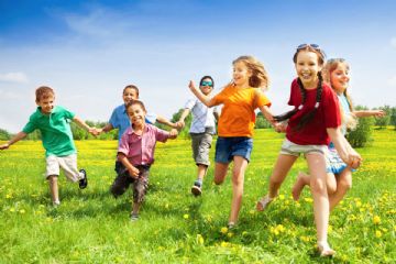 bambini che corrono in un giardino verde con fiori gialli
