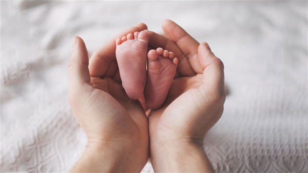 sfondo bianco, due mani di adulto che tengono due piedini di neonato